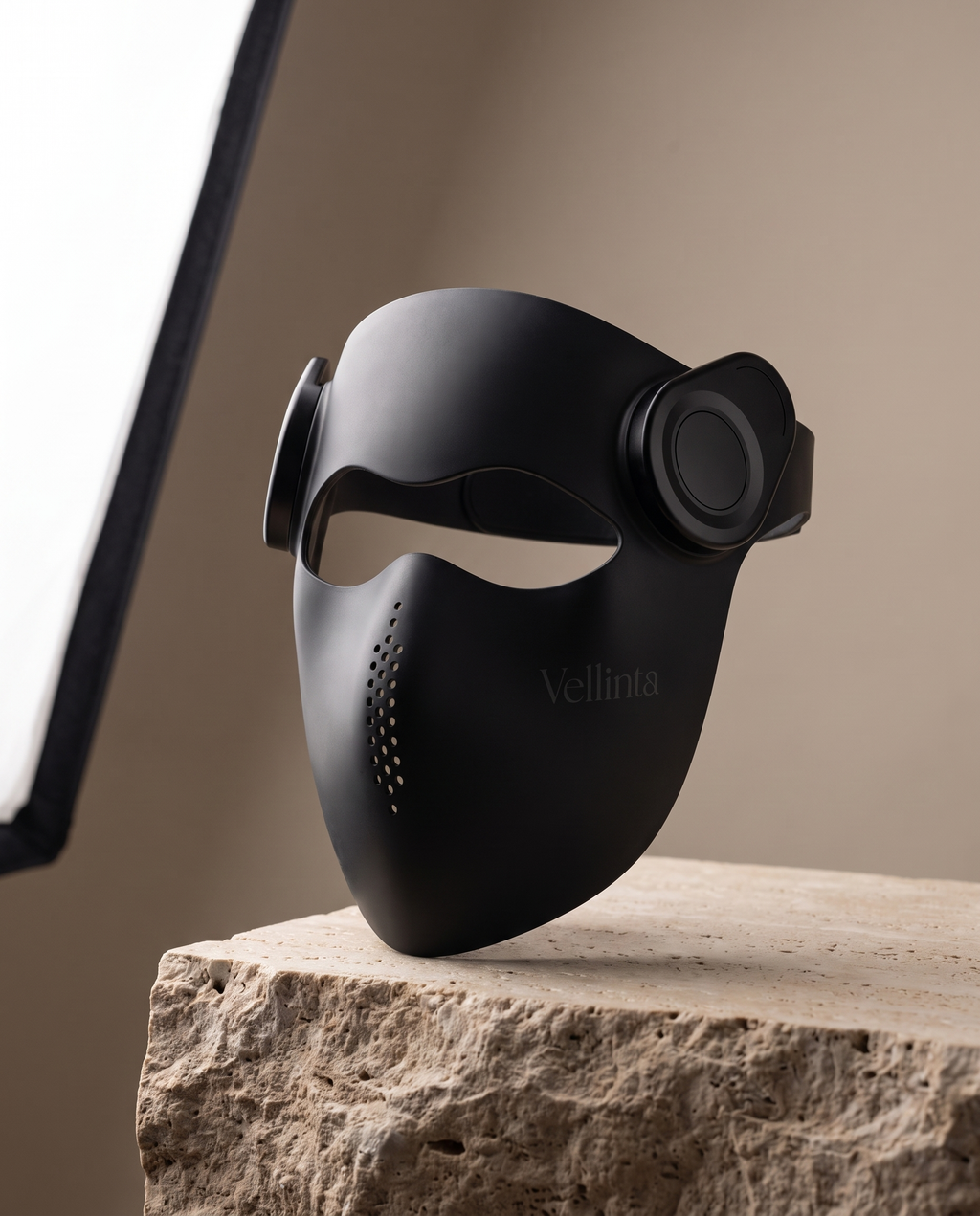 Vellinta Lumina Pro in Onyx, matte black LED face mask on a travertine stone plinth